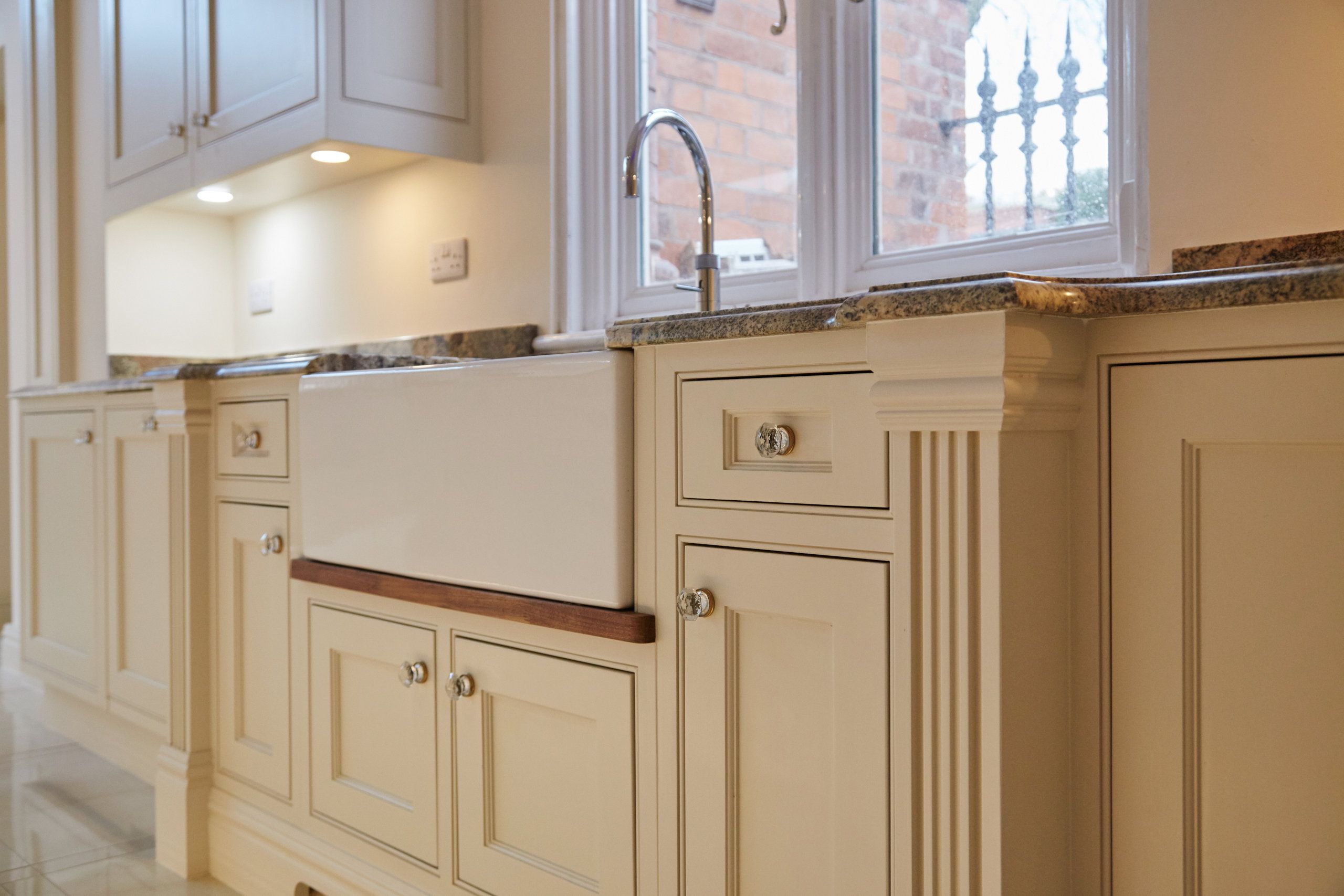 A large basin sink can be seen set in to the centre of a series of bespoke, traditional kitchen cabinets.