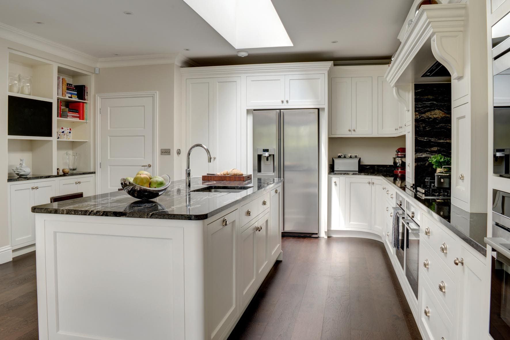 A bespoke traditional kitchen with white cabinets and black, granite worktops. A large skylight in the centre of the room bathes the kitchen in light.