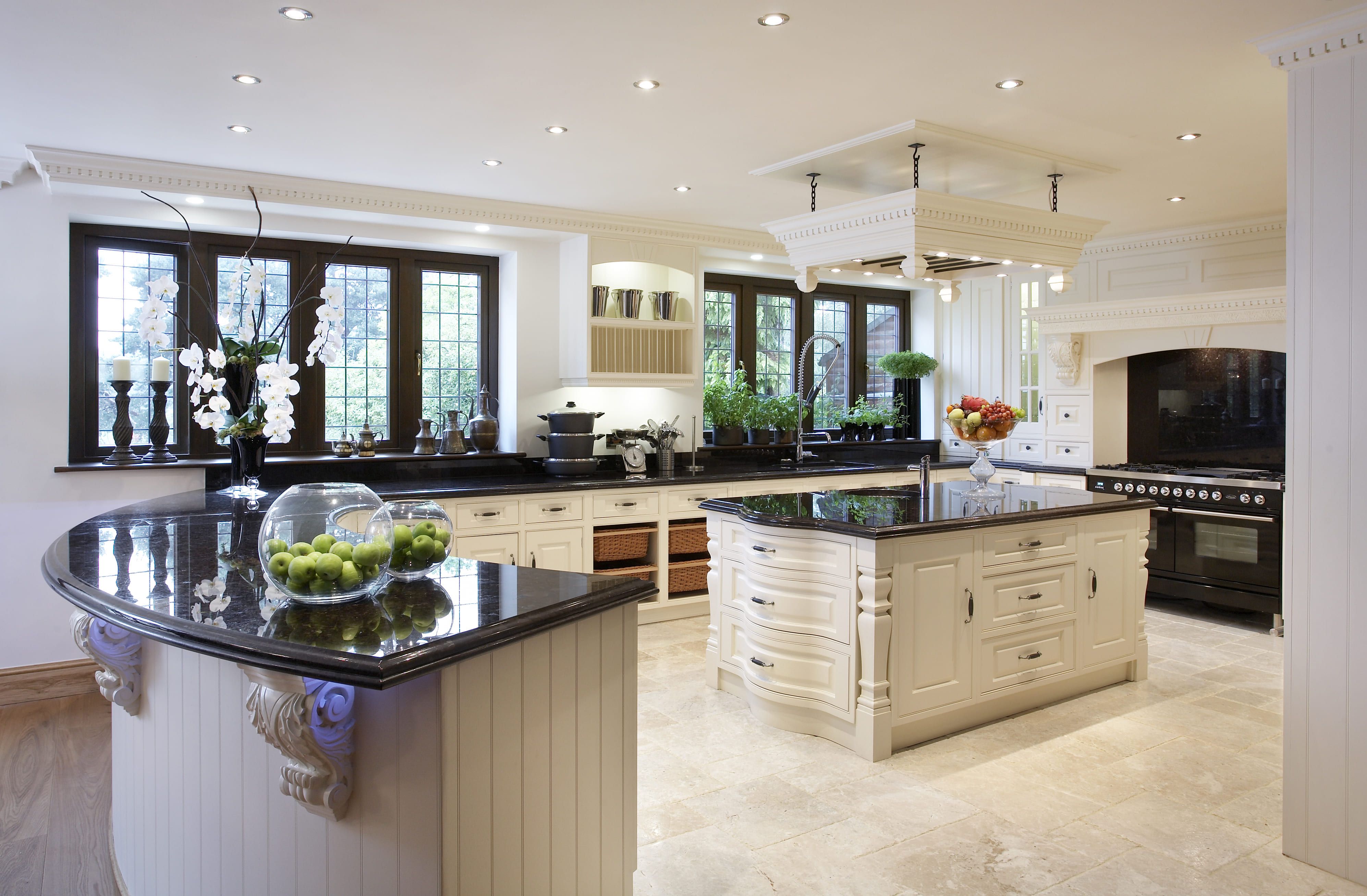 A spacious bespoke kitchen with cream panelled cabinetry, black granite worktops, a central island, and a traditional range cooker, all set against a backdrop of natural stone flooring and an ornate plastered ceiling.
