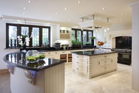A spacious bespoke kitchen with cream panelled cabinetry, black granite worktops, a central island, and a traditional range cooker, all set against a backdrop of natural stone flooring and an ornate plastered ceiling.