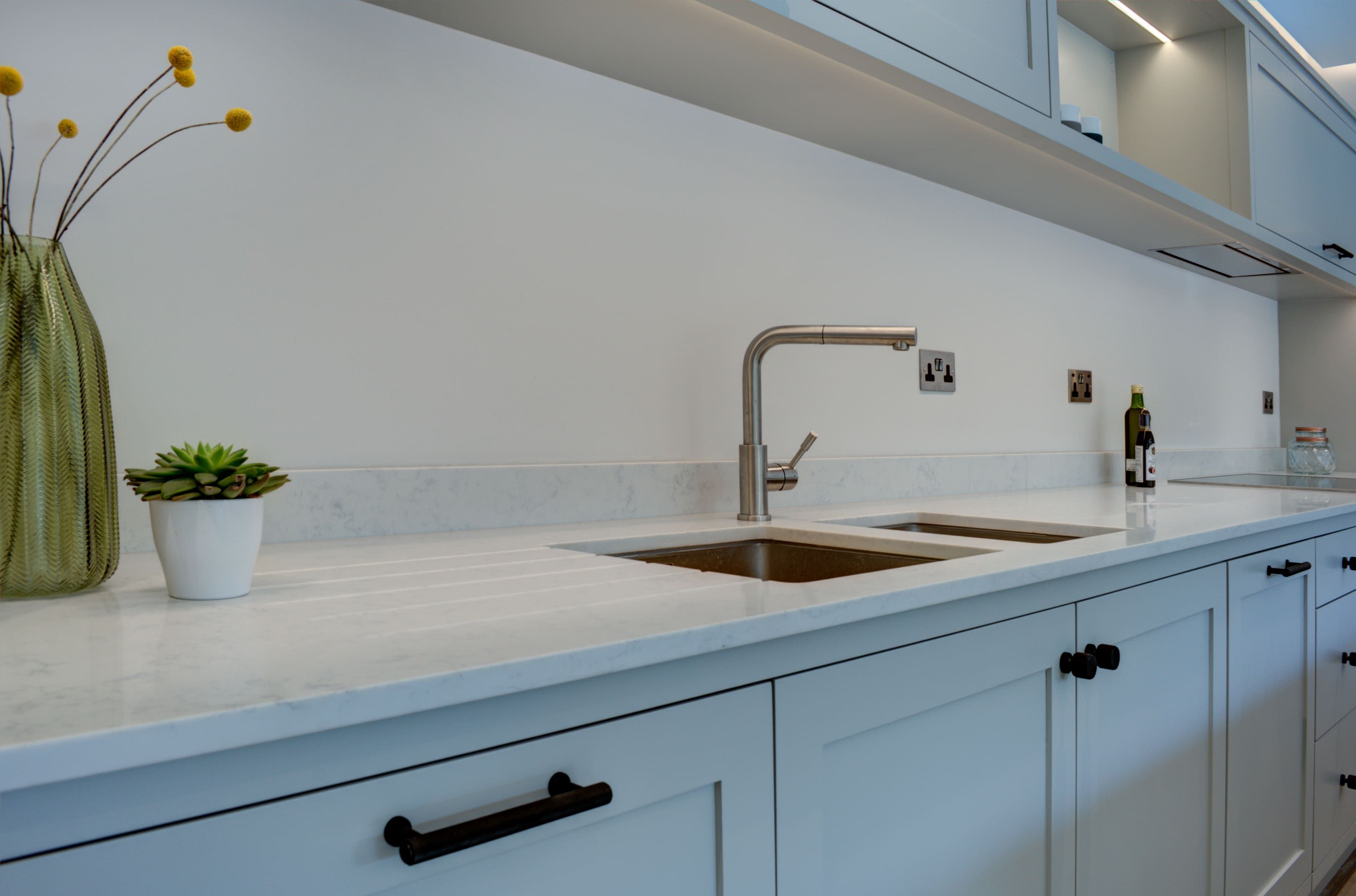 green plants and vases on a worktop provide contrast to a sleek, monotone white bespoke kitchen.