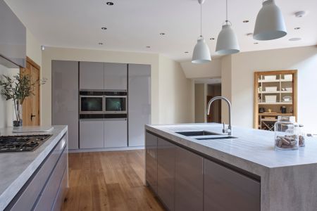 A minimalist bespoke kitchen with sleek grey cabinetry, a concrete effect island, natural wood flooring, and modern pendant lighting, creating a clean and airy space.