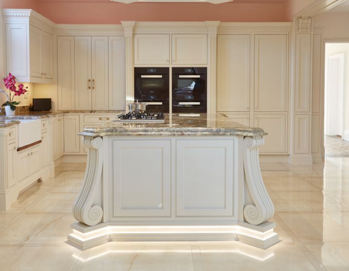A luxurious, bespoke traditional kitchen with cream cabinets, marble countertops, under-cabinet lighting, and built-in ovens.
