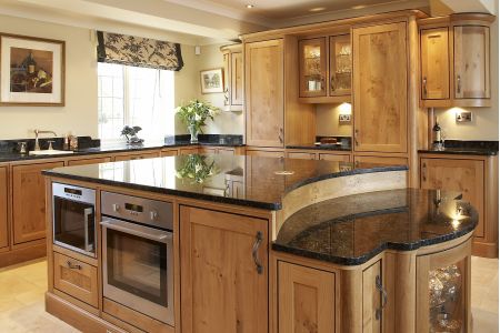 A traditional bespoke kitchen with natural wood cabinetry, black granite countertops, and built-in stainless steel appliances, complemented by under-cabinet lighting and a view to the garden.