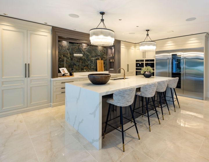 A bespoke traditional kitchen featuring a marble-topped island with bar stools, elegant twin pendant lights, and integrated high-end appliances, set against a backdrop of polished marble flooring.