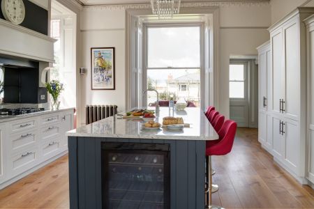 A large, navy blue, bespoke Shaker kitchen island with a grey marble worktop. Red stools provide some strong contrast and bring more colour to the room.