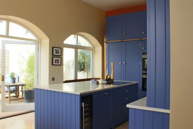 A striking blue, modular shaker kitchen with white counter tops is drowned in natural light from 2 large arched windows.