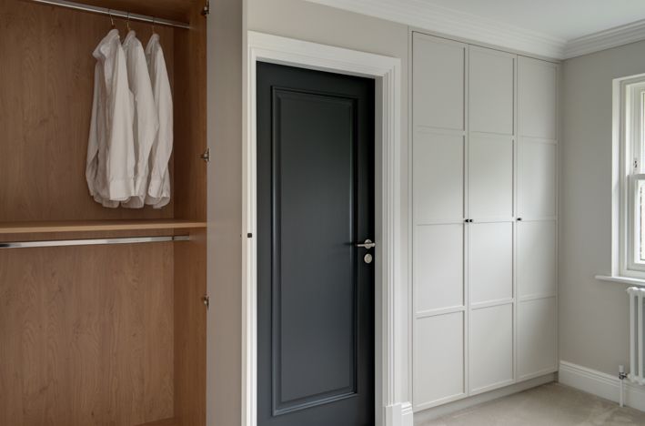 A minimalist bespoke dressing room. Grey cabinets line the wall, one is opened to show the functionality of the room.