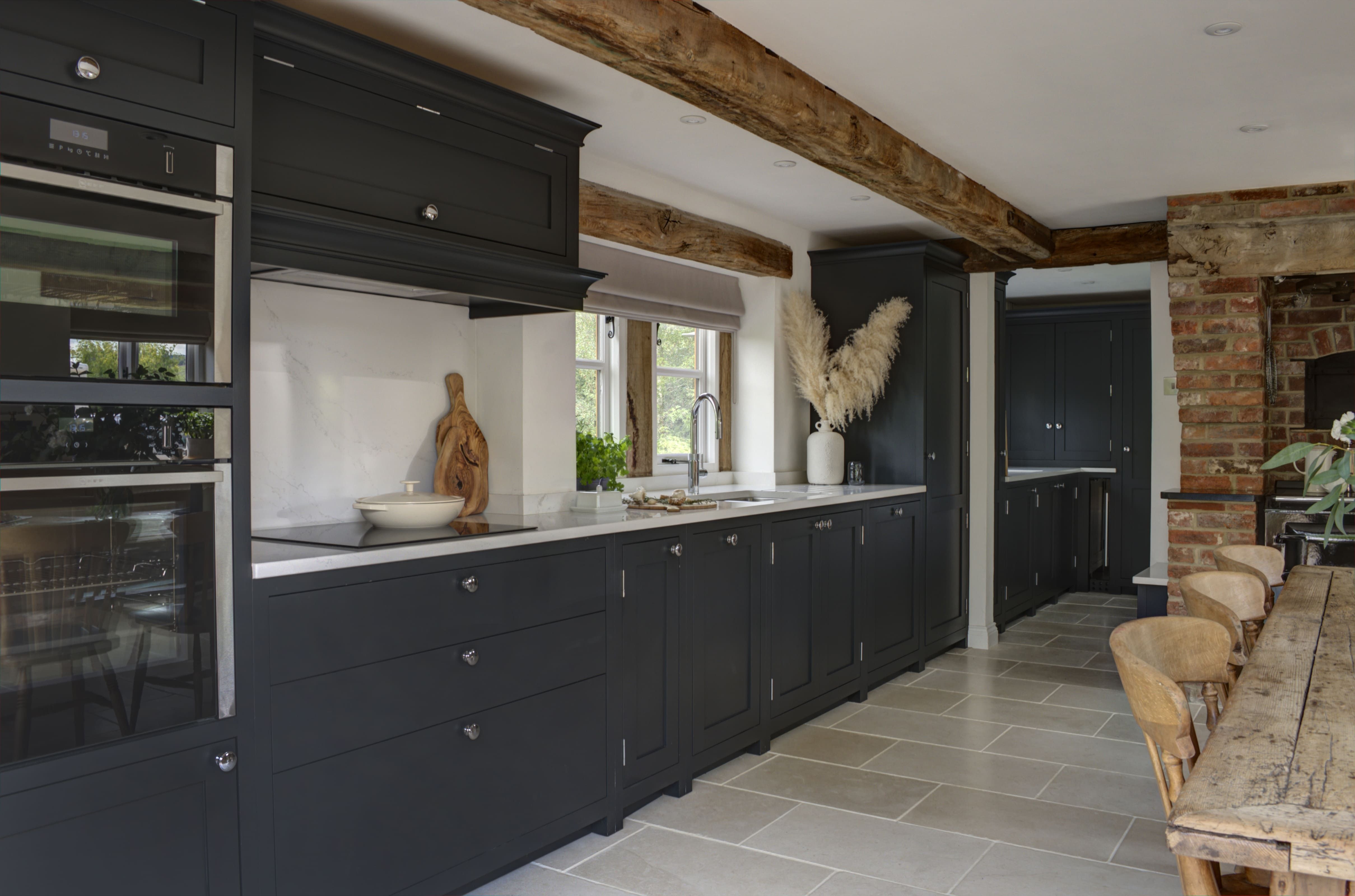 Exposed beams and brick walls provide an elegant contrast to the bespoke kitchen cabinets with white counter tops.