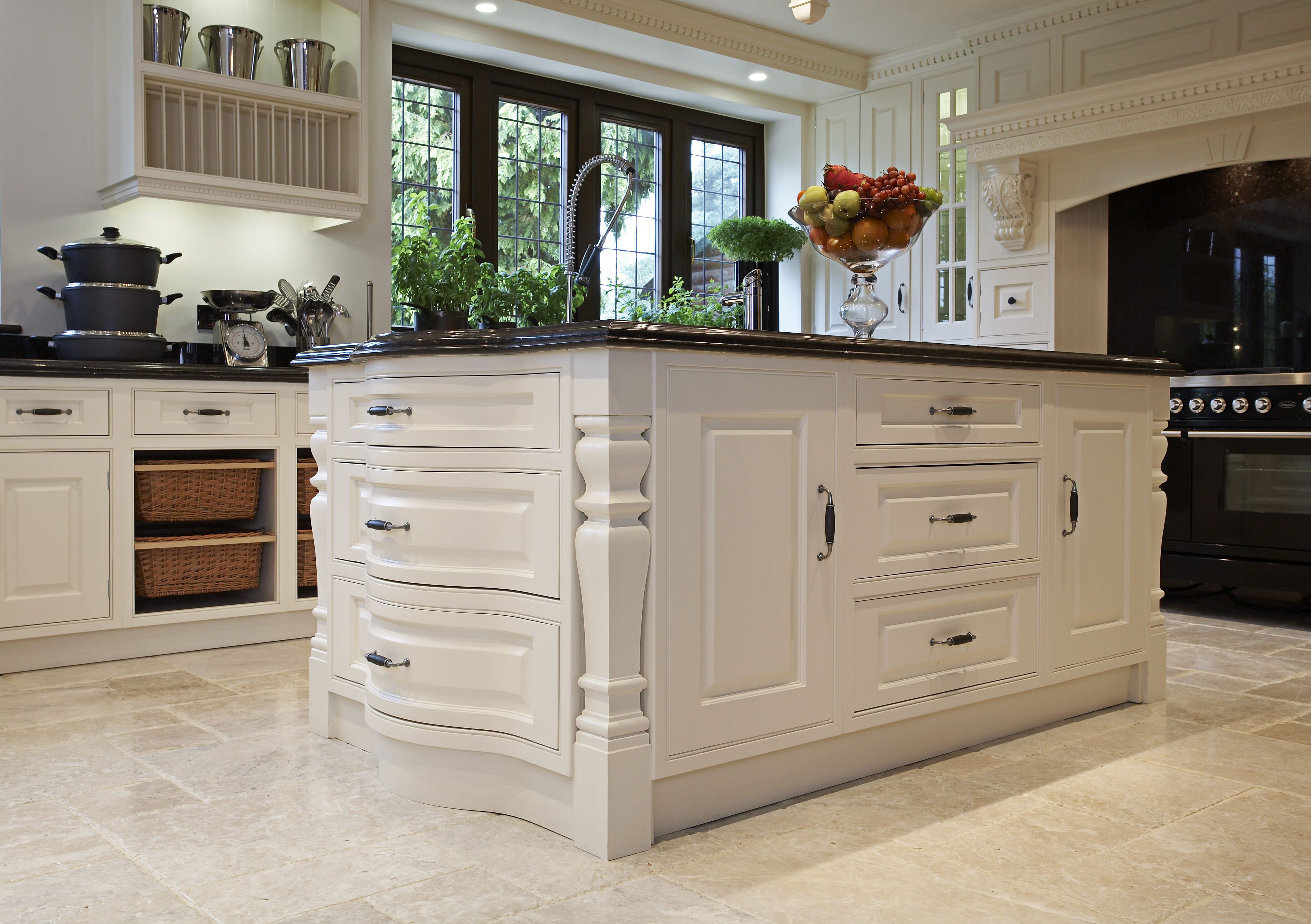 An ornate, bespoke kitchen island, white cabinets and a black worktop make up a striking piece.