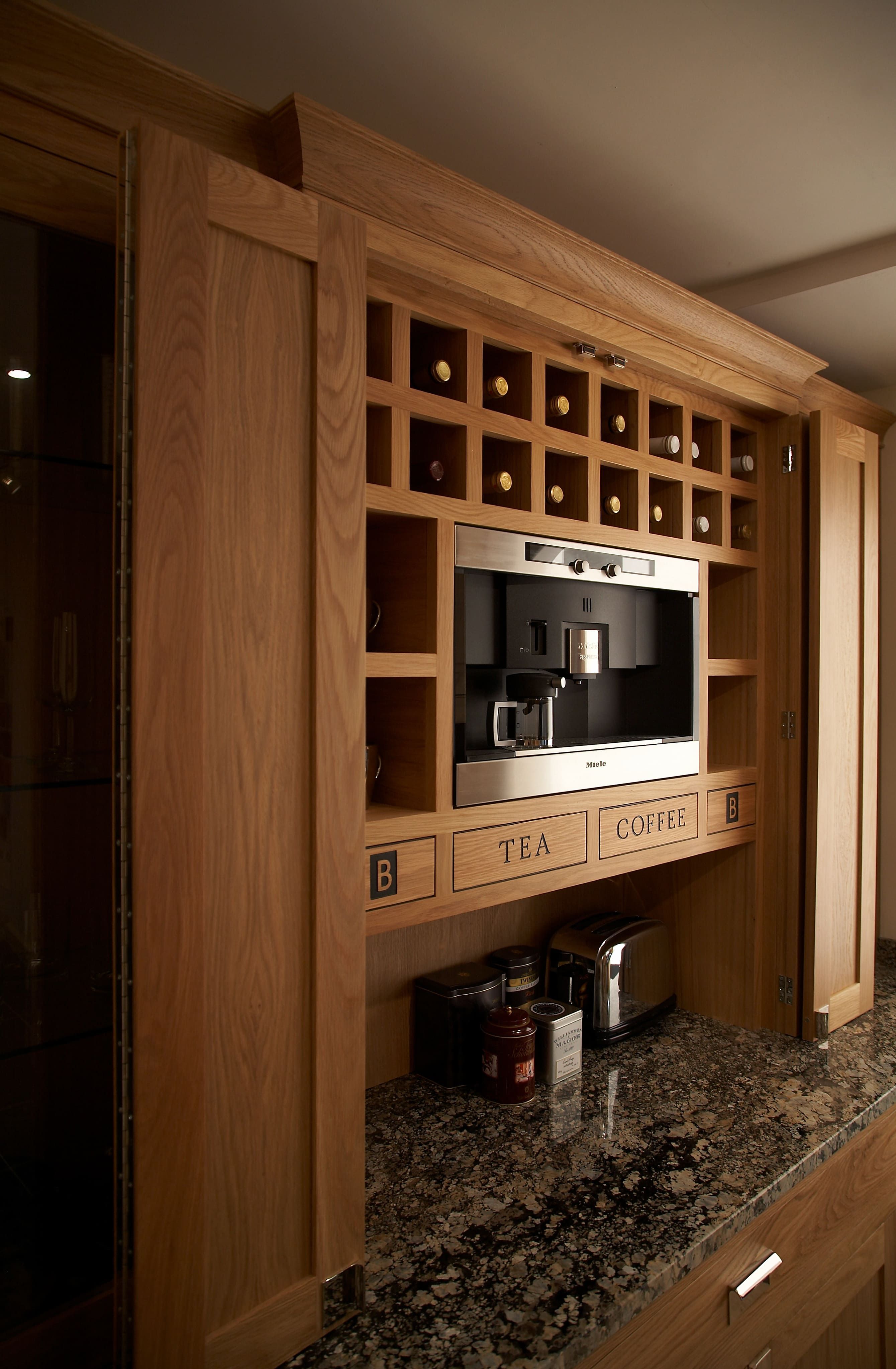 A bespoke, wooden open cabinet, featuring a wine rack. Set above a dark marble worktop.