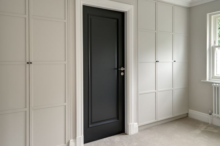 Built around a black internal door, are light-grey, floor-to-ceiling bespoke dressing room cabinets.