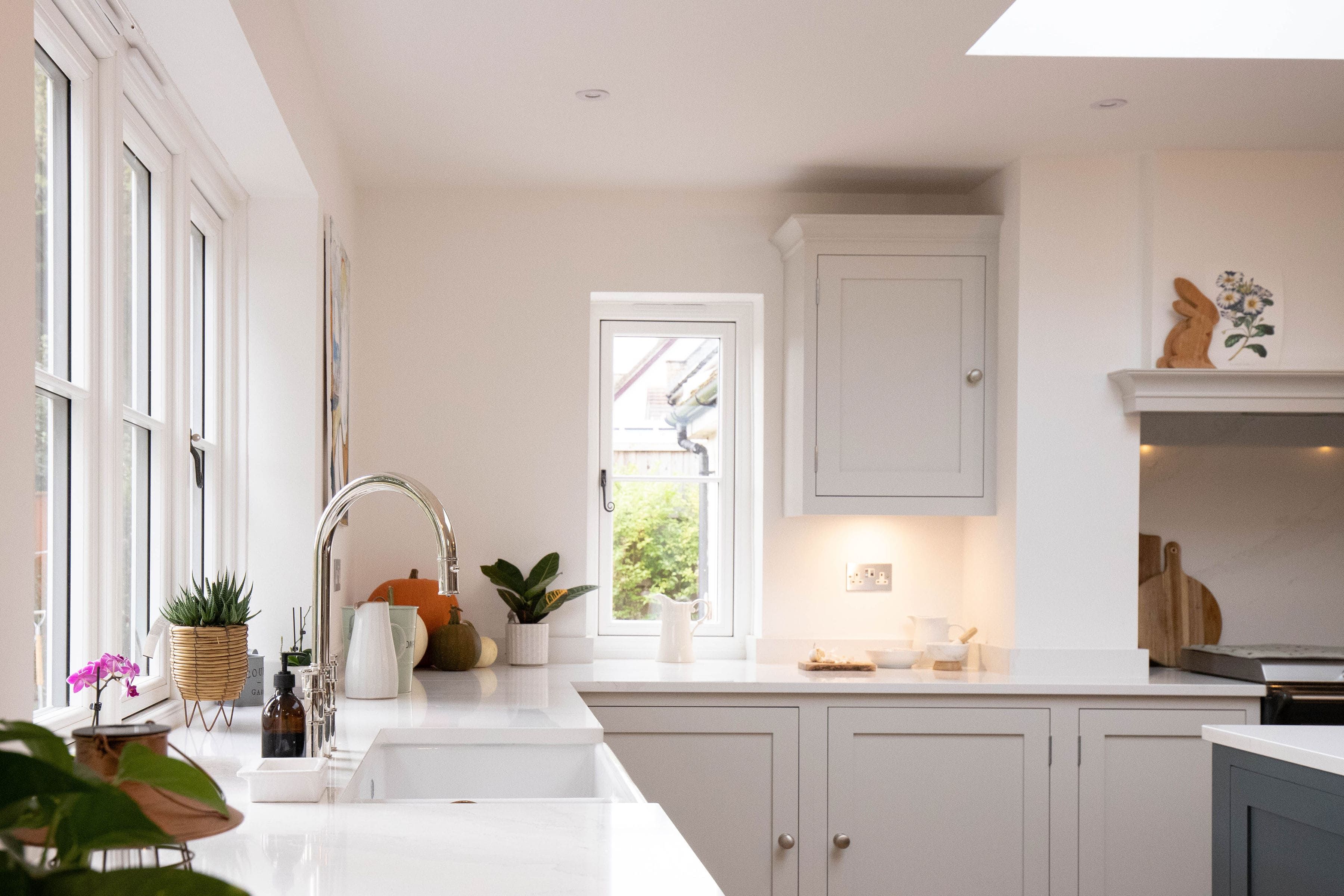 A bright, contemporary bespoke kitchen. A number of green plants are dotted around the work surface, bringing additional colour and contrast to the room.