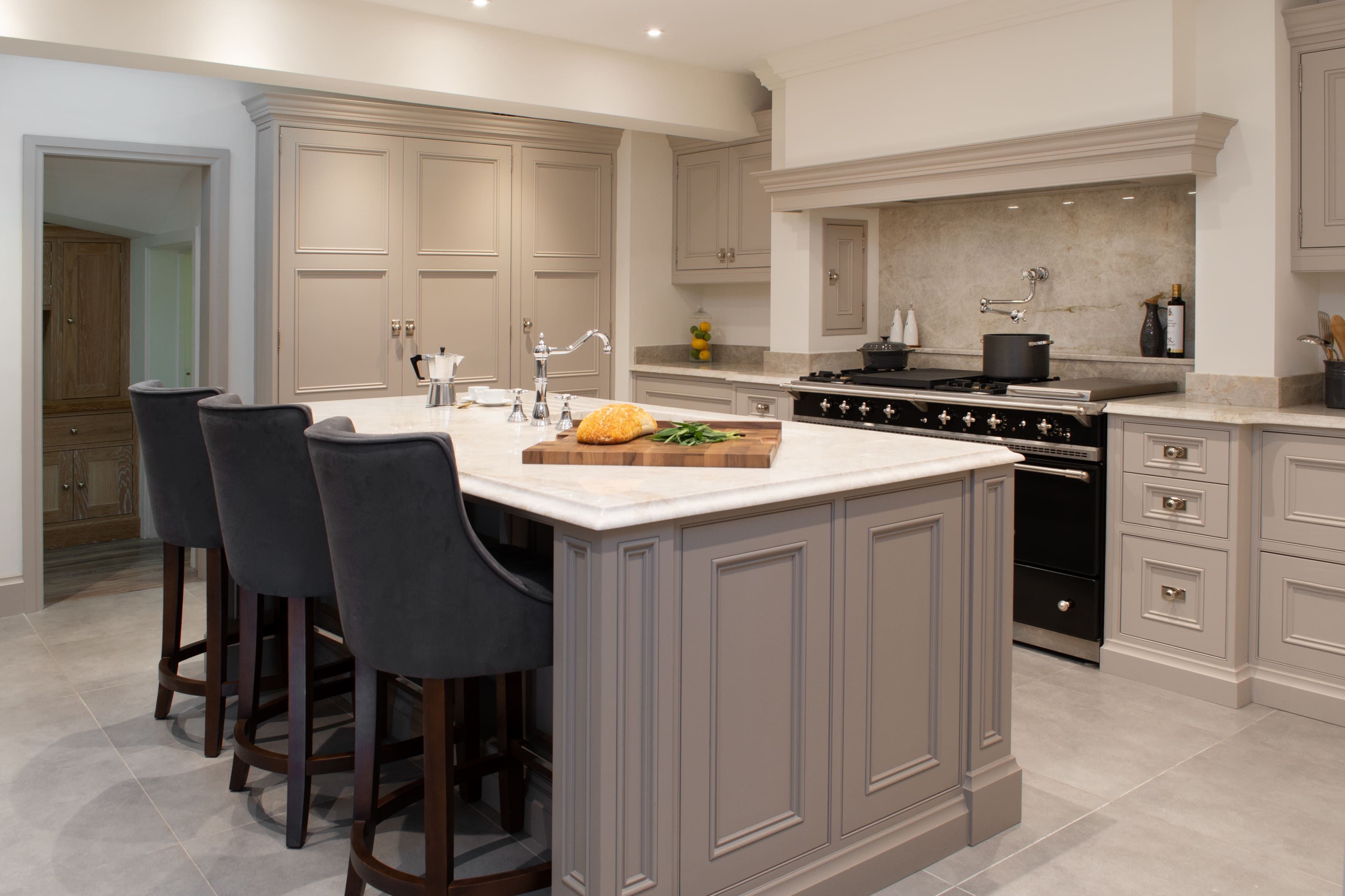 A grey-based, bespoke kitchen island. A large gas-top stove can be seen on the back wall, surrounded by shaker-style cabinets.