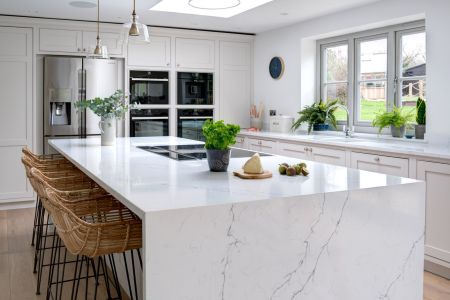 A bespoke shaker kitchen with a marble waterfall worktop and white cabinets.