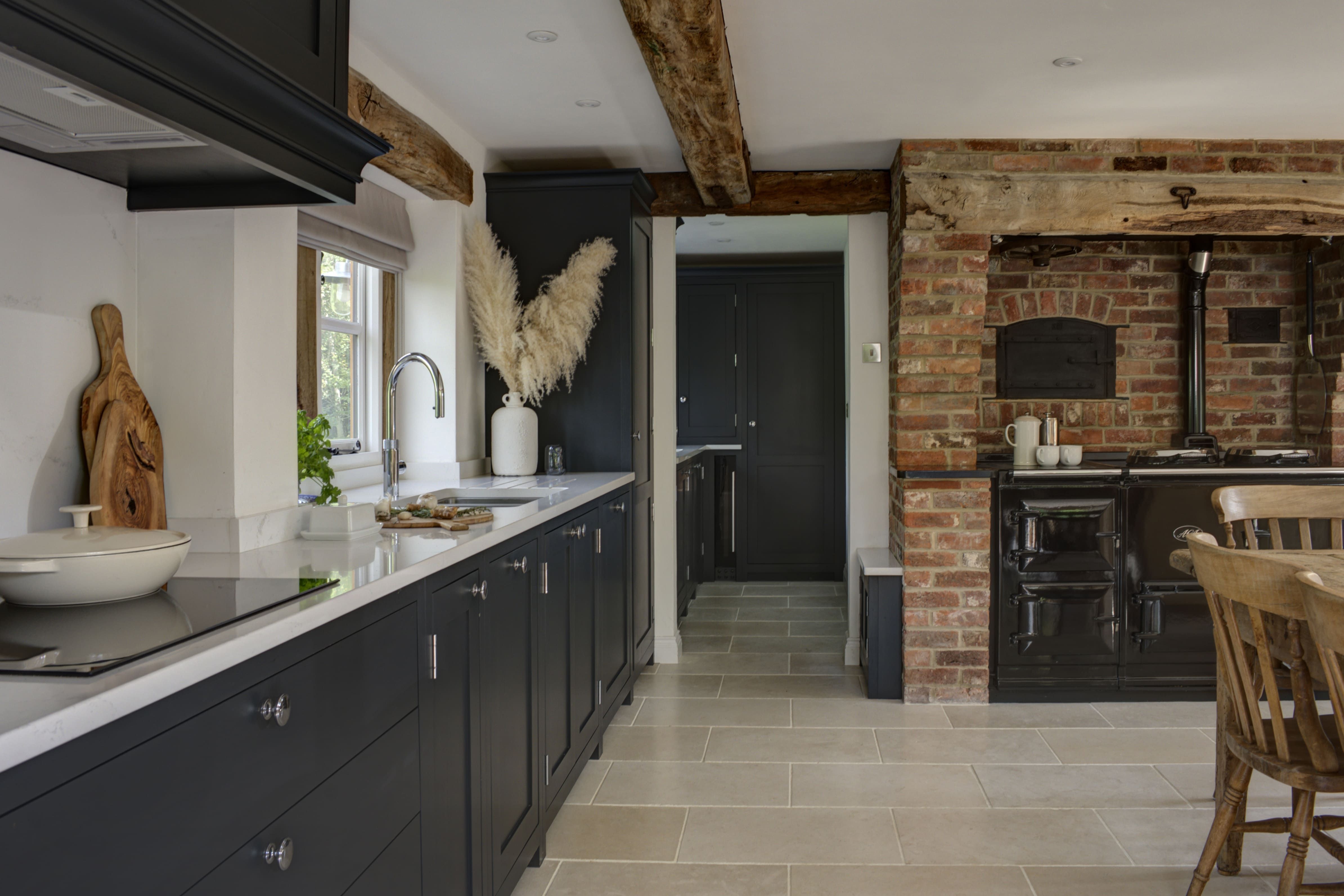 a rustic interior, with exposed oak beams and brick walls is contrasted by a dark blue, bespoke shaker kitchen with with counter tops.