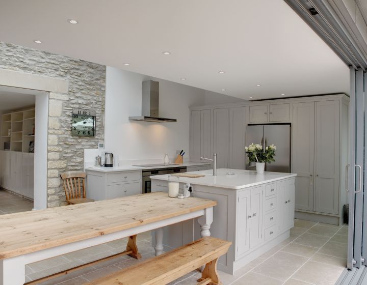 A light grey, bespoke shaker kitchen with centre island. A large table makes a rustic dining area.
