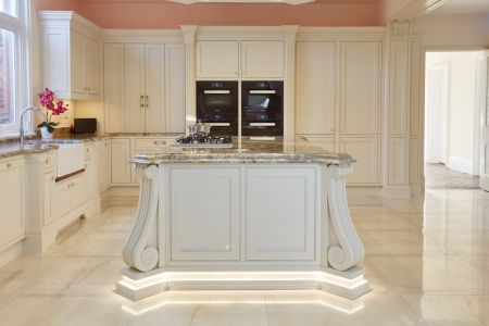 A luxurious, bespoke traditional kitchen with cream cabinets, marble countertops, under-cabinet lighting, and built-in ovens.