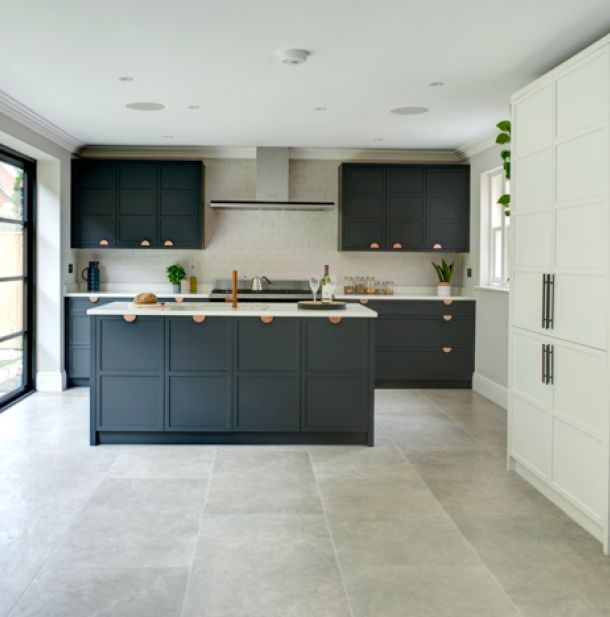 A bespoke contemporary kitchen with dark blue cabinets are contrasted by white painted brick walls and white countertops. Hints of bronze from the cabinet fittings provide some strong contrast.