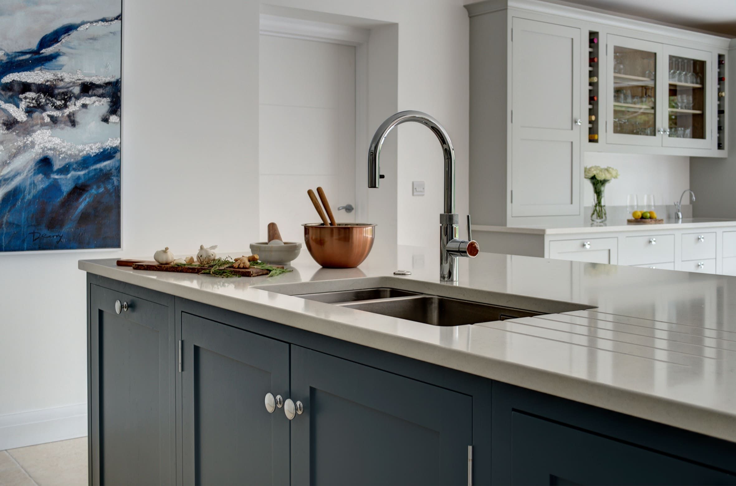An integrated sink is shown built in to a bespoke kitchen island with a cream-marble worktop. 