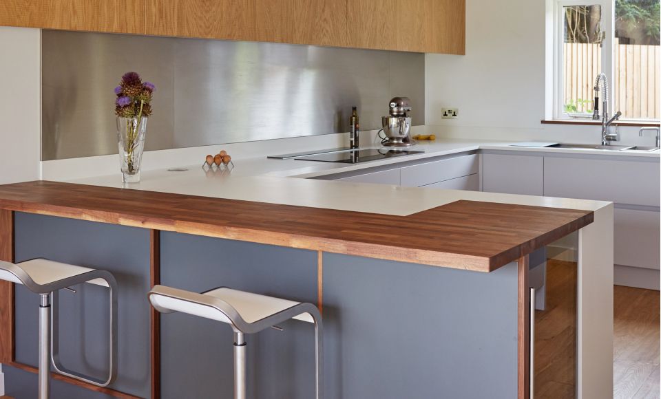 A bespoke contemporary kitchen, featuring grey cabinets and a hardwood surface. The room is bathed in natural light.