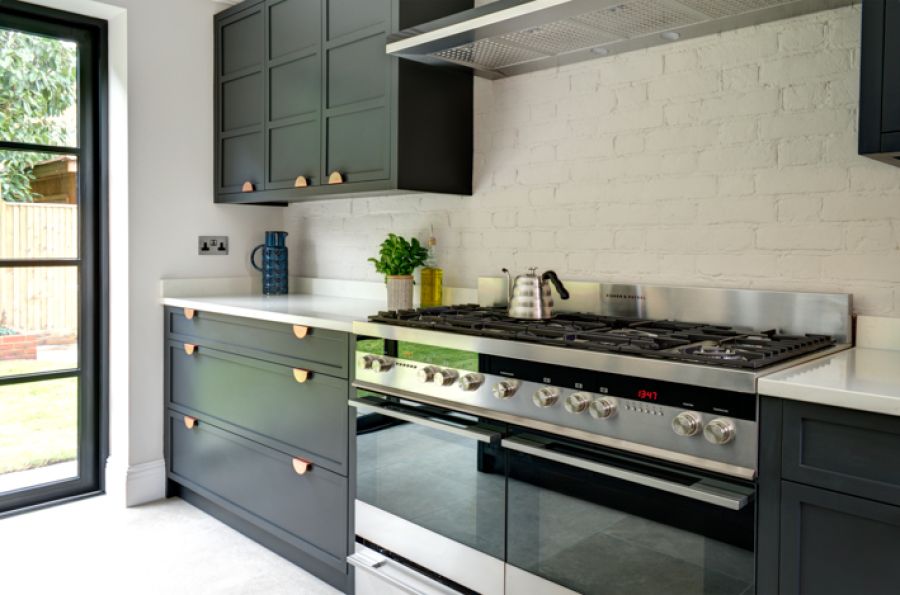 A bespoke contemporary kitchen with dark blue cabinets are contrasted by white painted brick walls and white countertops. Hints of bronze from the cabinet fittings provide some strong contrast.