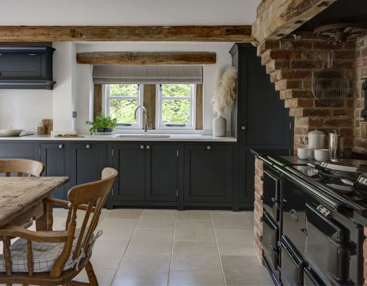 A rustic interior, with exposed oak beams and brick walls is contrasted by a dark blue, bespoke shaker kitchen with with counter tops.