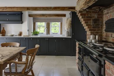 A rustic interior, with exposed oak beams and brick walls is contrasted by a dark blue, bespoke shaker kitchen with with counter tops.