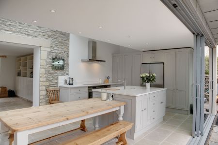 A light grey, bespoke shaker kitchen with centre island. A large table makes a rustic dining area.